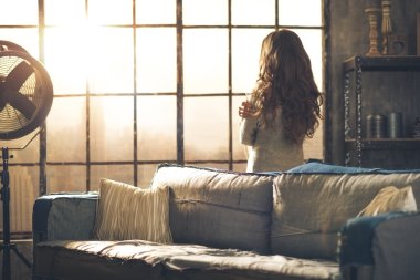 Brunette looking out of urban loft window clipart