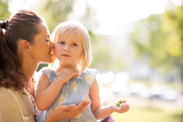 Mutter flüstert ihrer Tochter in der Sonne im Stadtpark zu — Stockfoto