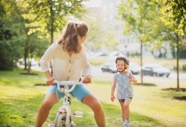 Μητέρα παιχνιδιάρικα ποδήλατο ένα ξανθό κορίτσι σε ένα ηλιόλουστο πάρκο — Φωτογραφία Αρχείου