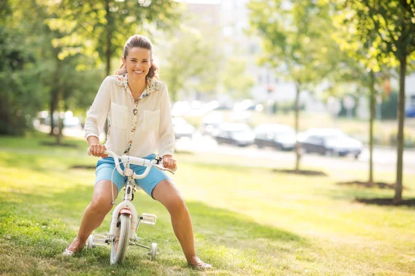 Mother pretending to ride a child's bike in a sunny city park — Stock Photo, Image