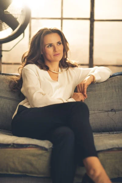 Mujer elegante sentada en un sofá en un loft mirando a la distancia — Foto de Stock