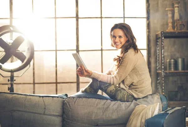 Smiling woman sitting on back of sofa looking up from table pc — Stock Photo, Image