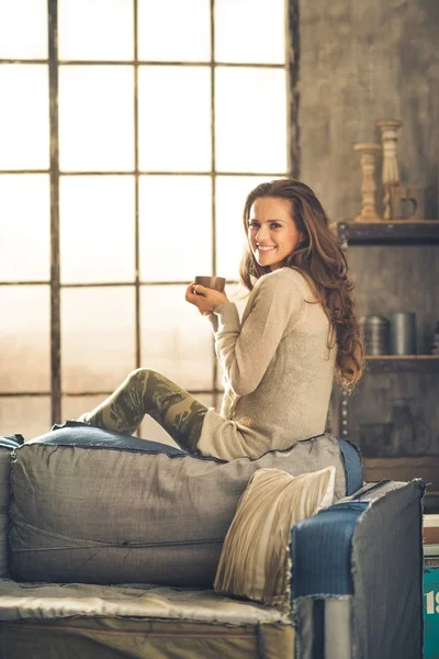 Vrouw die lacht kijken over de schouder houden cup in loft — Stockfoto