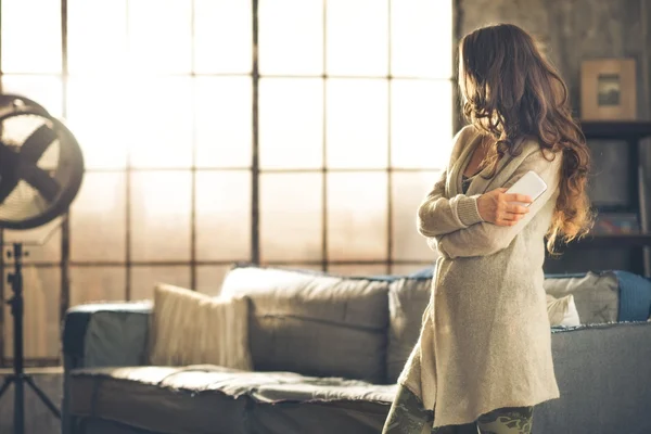 Brunette looking away holding phone in a loft apartment — Stock Photo, Image