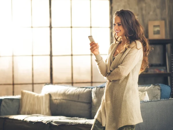 Женщина смотрит в сторону держа телефон стоя в квартире чердак — стоковое фото