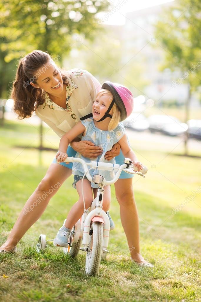 Laughing mother holding daughter on bike in a sunny city park Stock Photo  by ©CITAlliance 72933607