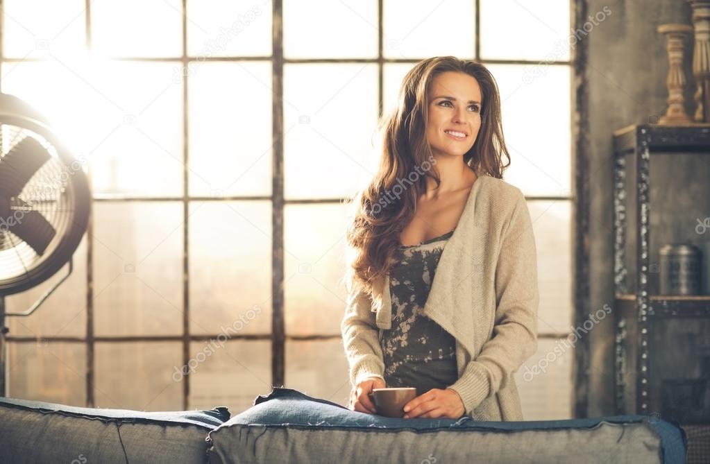 Casual brunette with coffee smiling in loft apartment