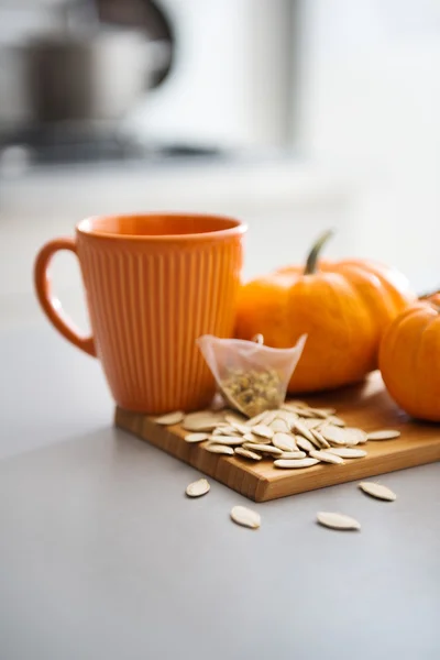 Tasse de couleur citrouille avec citrouilles miniatures et graines à bord — Photo