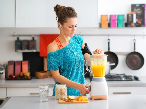 Adatta donna in attrezzi da allenamento in cucina facendo un frullato — Foto Stock