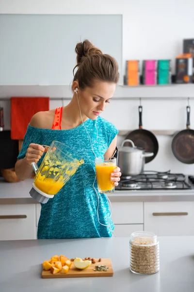 Mulher em equipamento de treino derramando smoothie na cozinha — Fotografia de Stock