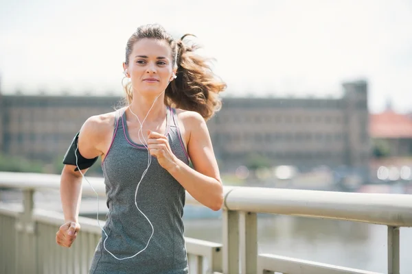 Smiling woman jogging in urban setting listening to music — Stock Photo, Image