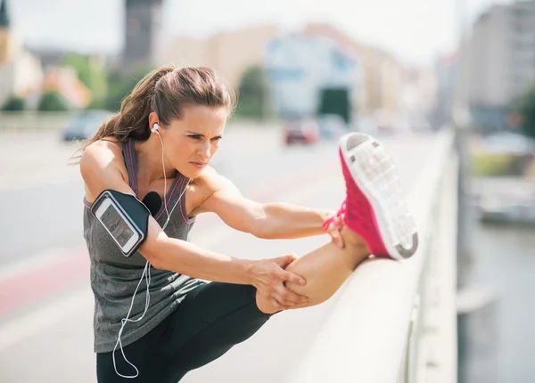 Woman runner stretching leg on rail in summer in urban setting — Stock Photo, Image