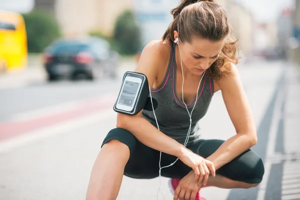 Woman runner kneeling, looking down, listening to music — Stock Photo, Image