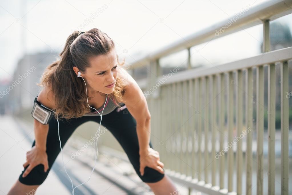 Woman jogger stretching on bridge while listening to music