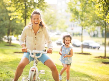 Anne ve bebek kız parkta bisiklet ile eğleniyor