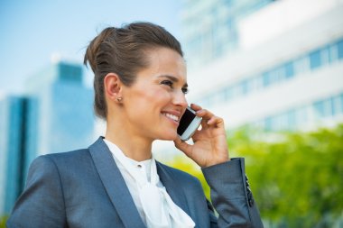 Smiling business woman talking cell phone in front of office bui