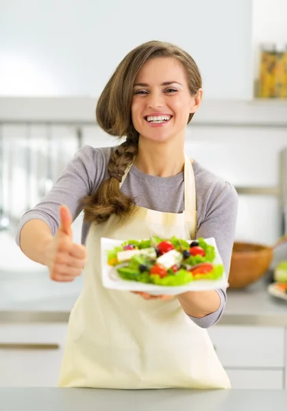 Jovem dona de casa feliz mostrando salada grega e polegares para cima — Fotografia de Stock