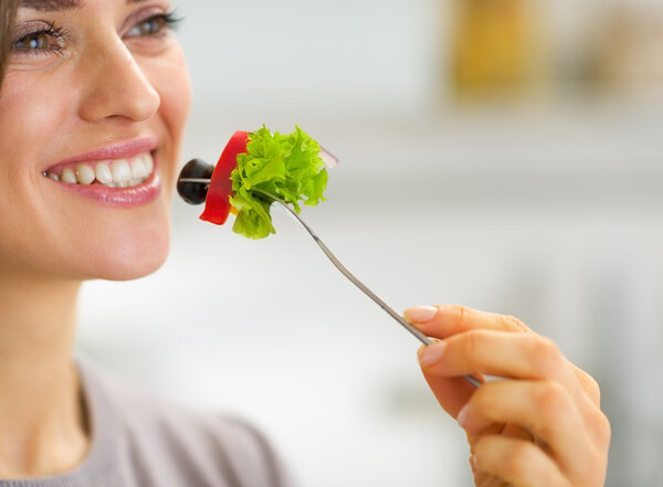 Closeup on happy young housewife eating vegetables