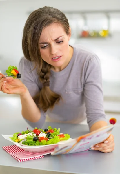 Jonge vrouw eten Griekse salade in keuken en lezing tijdschrift — Stockfoto