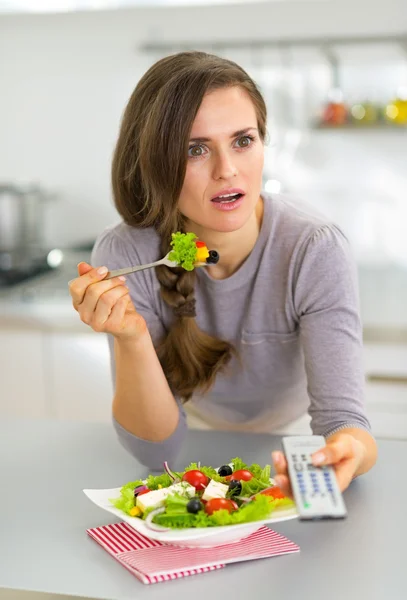 Sorprendido joven mujer comiendo ensalada griega y viendo la televisión —  Fotos de Stock