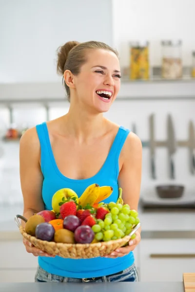 Χαμογελώντας νεαρή γυναίκα με πλατώ φρούτων στην κουζίνα — Φωτογραφία Αρχείου
