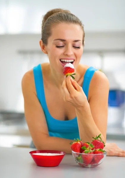Glückliche junge Frau isst Erdbeere mit Joghurt in Küche — Stockfoto