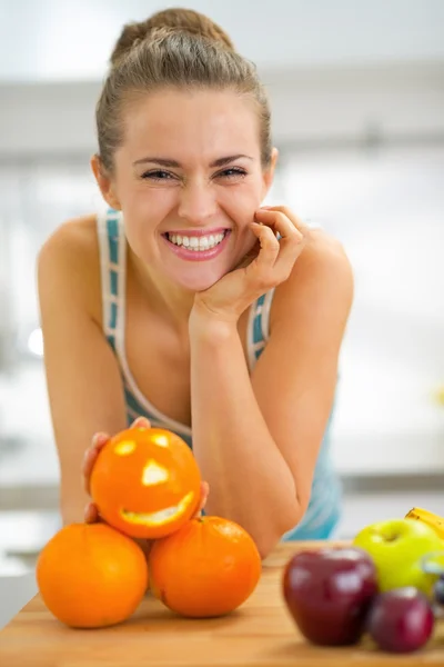 Retrato de jovem feliz com laranja halloween na cozinha — Fotografia de Stock