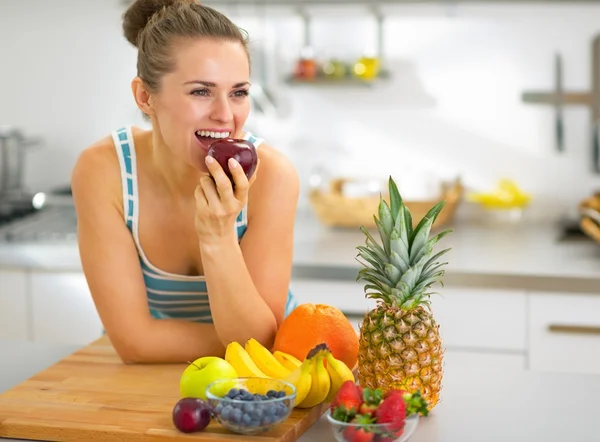 Jovem mulher comendo maçã na cozinha — Fotografia de Stock