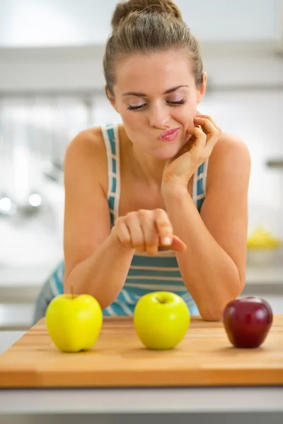 Задумчивая молодая женщина выбирает между красными и зелеными яблоками — стоковое фото