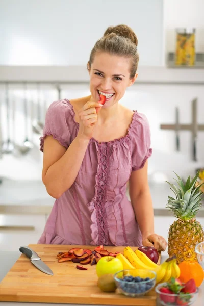 Retrato de feliz jovem dona de casa comendo morango ao fazer — Fotografia de Stock