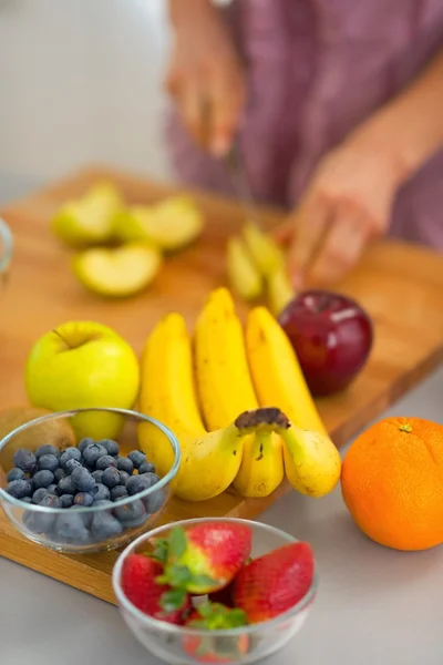 Closeup on fruits and young housewife cutting in background — Stock Photo, Image