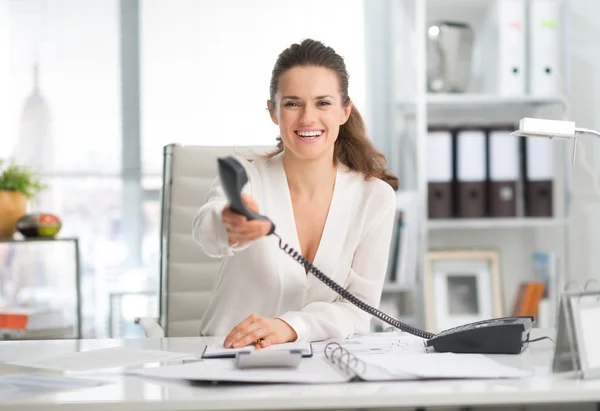 Mujer de negocios sonriente en el escritorio entregando teléfono —  Fotos de Stock