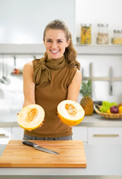 Lachende jonge vrouw meloen segmenten in keuken tonen — Stockfoto