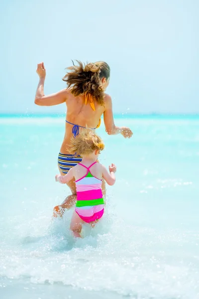 Deniz kıyısında oynayan kız anne ve bebek. arka görünüm — Stok fotoğraf
