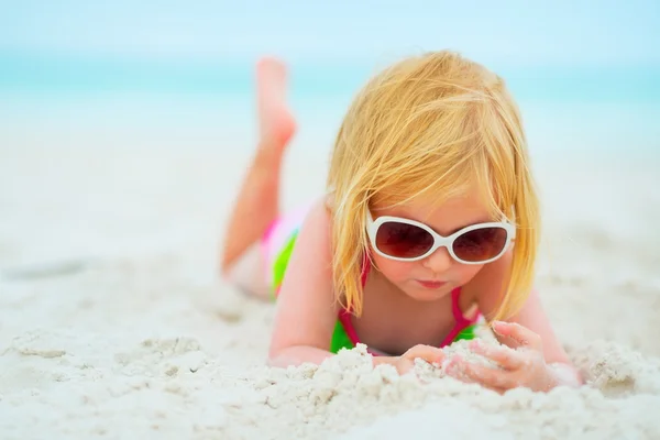 Baby girl in sunglasses laying on beach — Stock Photo, Image
