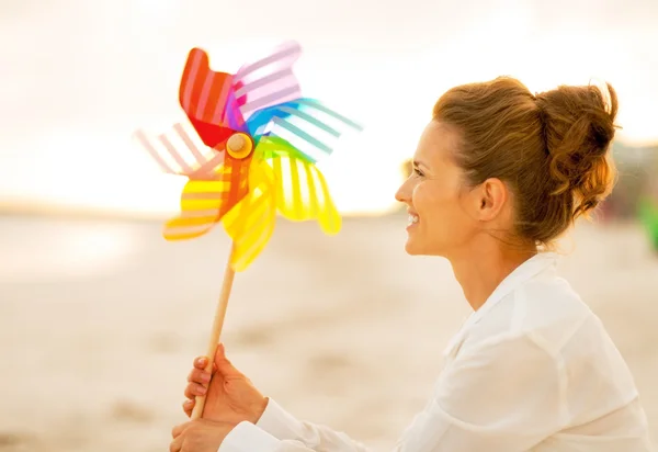 Feliz joven mujer con colorido molino de viento juguete sentado en la playa en —  Fotos de Stock
