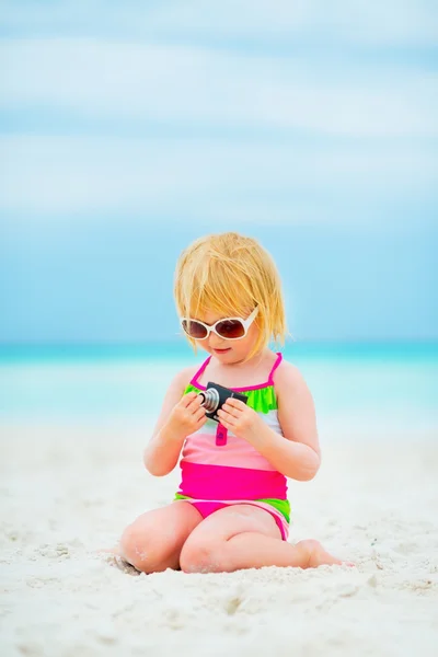 Liten jente i solbriller med fotokamera sittende på stranden – stockfoto