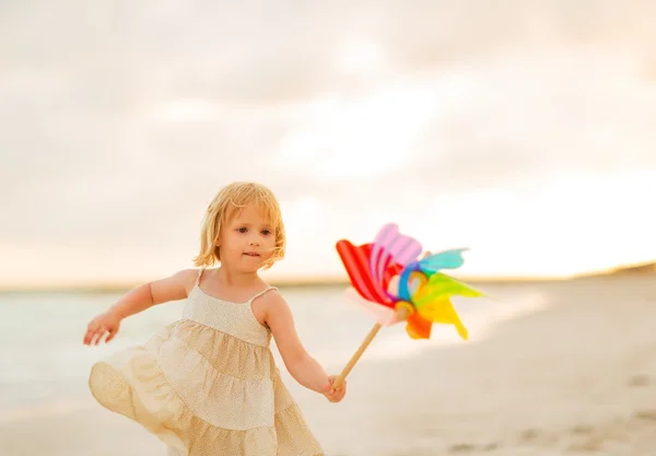 Holčička hraje s hračkou barevné větrný mlýn na pláži — Stock fotografie