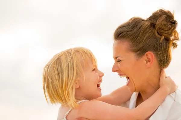 Portrait de mère riante et bébé fille étreignant sur la plage à th — Photo