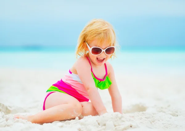 Niña sonriente en gafas de sol jugando con arena en la playa — Foto de Stock