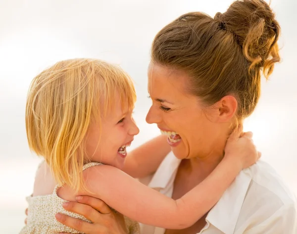 Porträt einer lächelnden Mutter und eines kleinen Mädchens, die sich am Strand am — Stockfoto