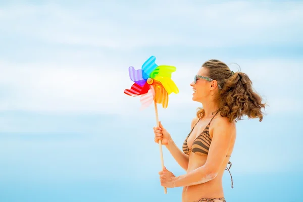 Happy young woman playing with colorful windmill toy on beach — Stock Photo, Image