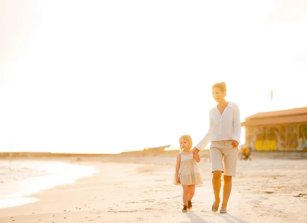 Glückliche Mutter und kleines Mädchen spazieren am Abend am Strand — Stockfoto