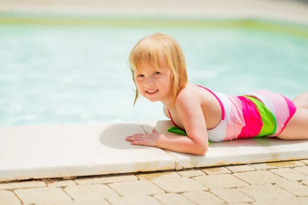 Meisje van de baby te leggen in de buurt van zwembad — Stockfoto