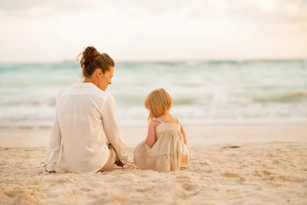 Mutter und Baby sitzen abends am Strand. Rückansicht — Stockfoto