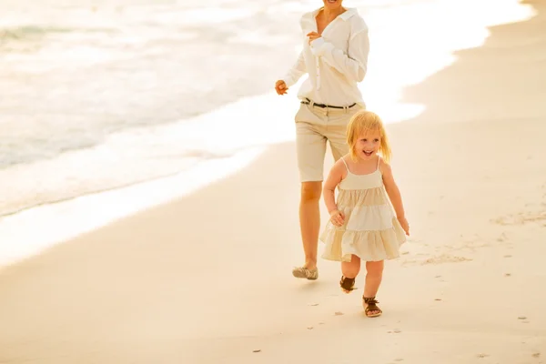 Mamma och baby flicka kör på stranden på kvällen — Stockfoto