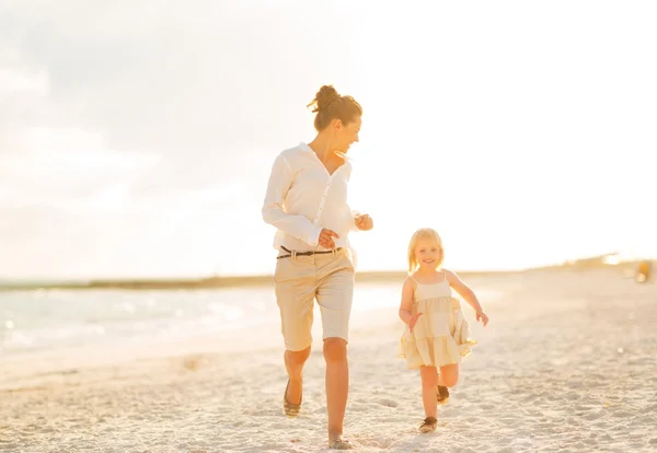 Glad mamma och baby flicka kör på stranden på kvällen — Stockfoto