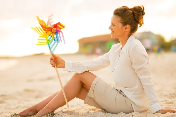 Glad ung kvinna med färgglada väderkvarnen leksak sitter på stranden vid — Stockfoto