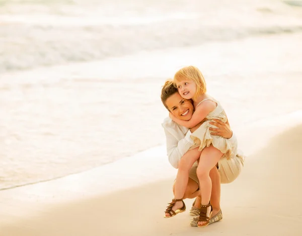 Moeder en baby meisje op strand glimlachen op de avond — Stockfoto