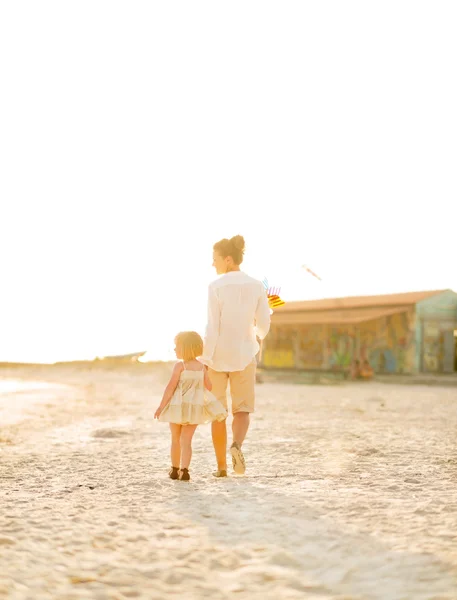 Matka i dziecko dziewczyna spaceru na plaży w godzinach wieczornych. widok z tyłu — Zdjęcie stockowe